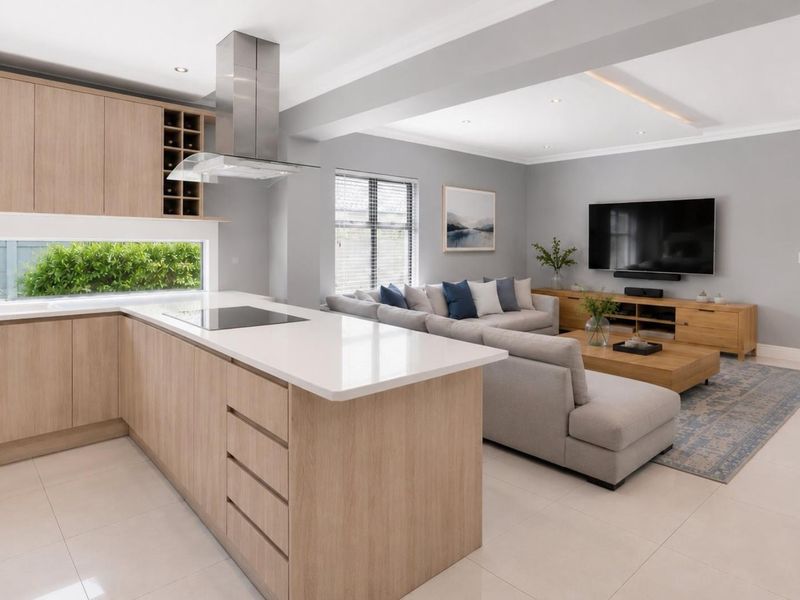 Modern open-plan living area featuring a sleek kitchen with light wood cabinetry, stone countertops, and seamless flow to the outdoor patio through bi-fold doors.