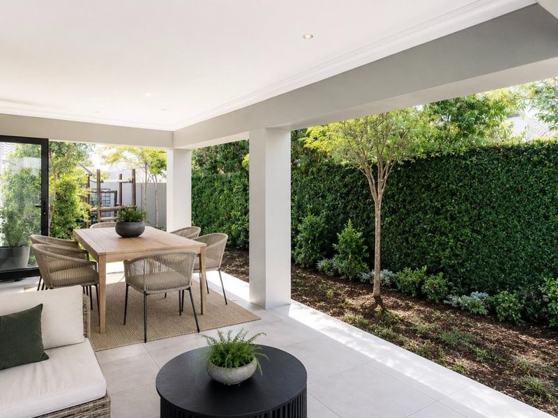 A covered outdoor patio featuring tiled flooring, recessed lighting, and bi-fold doors, providing a seamless transition to the landscaped garden area.