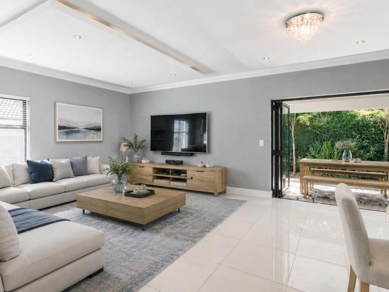 Spacious open-plan living area featuring high-gloss floor tiles, a recessed ceiling with feature lighting, and seamless bi-fold door access to the outdoor patio.