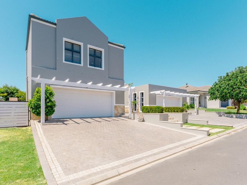 A modern double-story home featuring a paved driveway, double garage, and decorative pergola, set within a well-maintained residential street.