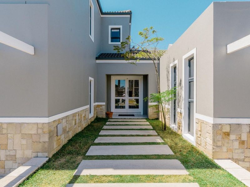Modern front entrance featuring stone cladding, a concrete paver walkway, and double glass doors leading into the home.
