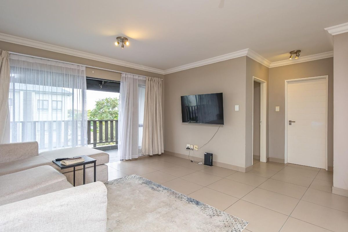 A bright and spacious living area featuring neutral tiled flooring, crown molding, and direct access to a private balcony through sliding glass doors.