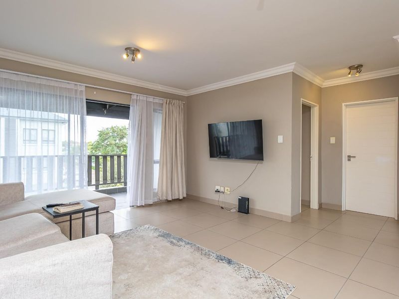 A bright and spacious living area featuring neutral tiled flooring, crown molding, and direct access to a private balcony through sliding glass doors.