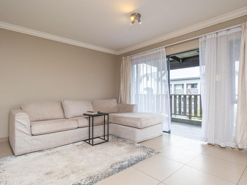 A bright living room featuring neutral tiled flooring, ceiling cornicing, and a large sliding glass door providing access to an outdoor balcony.