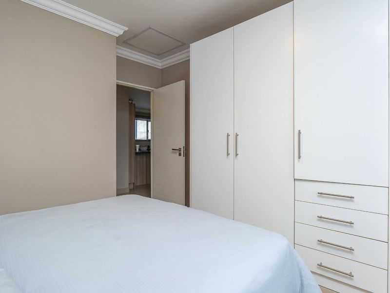 A well-maintained bedroom featuring neutral walls, crown molding, and ample built-in cupboard storage with integrated drawers.