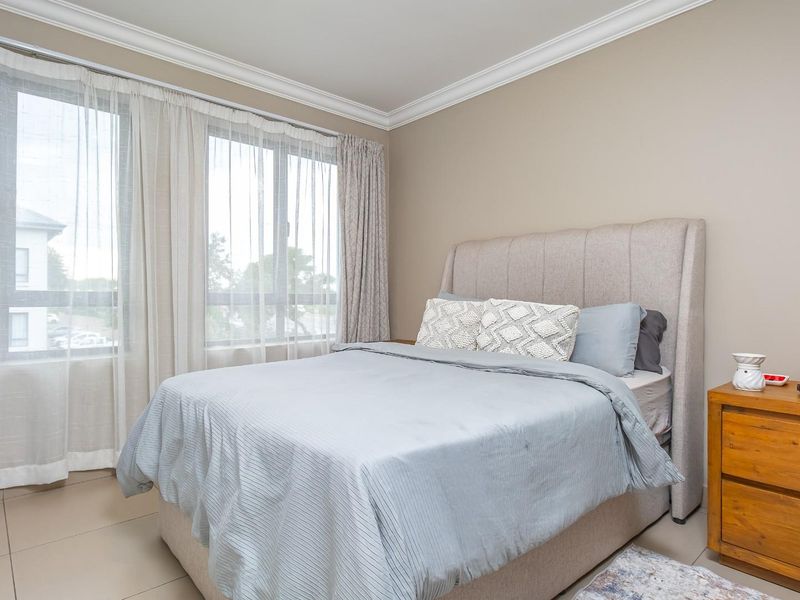 A well-lit bedroom featuring large windows, crown molding, and neutral tiled flooring, providing a comfortable and bright living space.