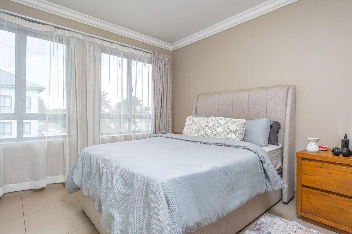 A well-lit bedroom featuring large windows, crown molding, and neutral tiled flooring, providing a comfortable and bright living space.