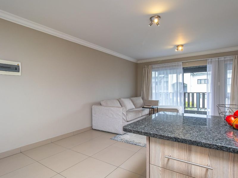 Open-plan living area featuring tiled flooring, a granite-topped kitchen island, and sliding door access to a balcony.