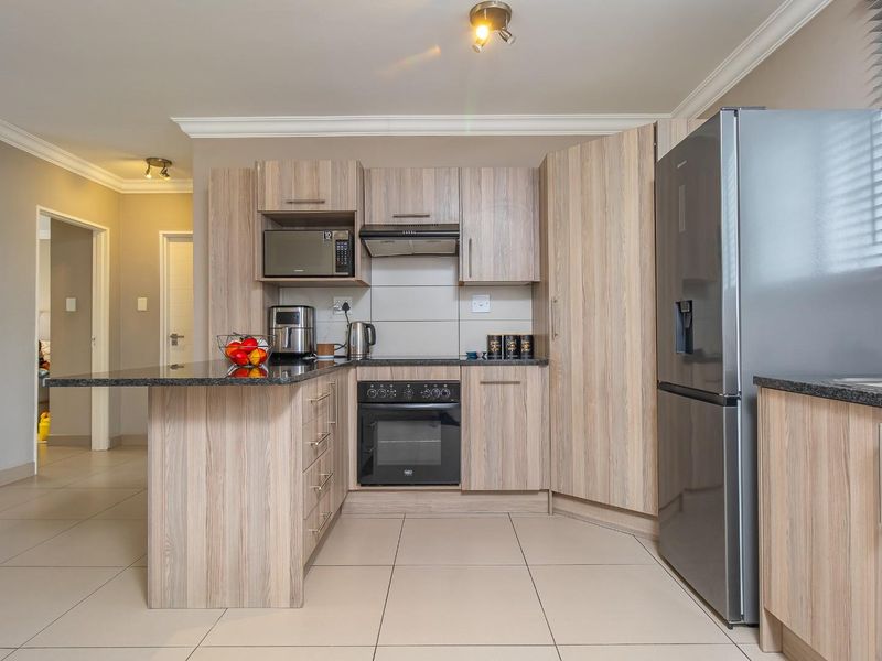 Modern kitchen featuring light wood-grain cabinetry, granite countertops, built-in oven, extractor fan, and tiled flooring in an open-plan layout.