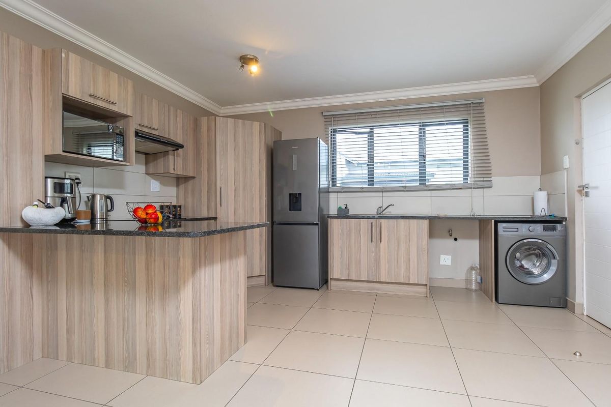 Modern kitchen featuring light wood-grain cabinetry, granite countertops, integrated microwave, extractor fan, and tiled flooring with space for laundry appliances.