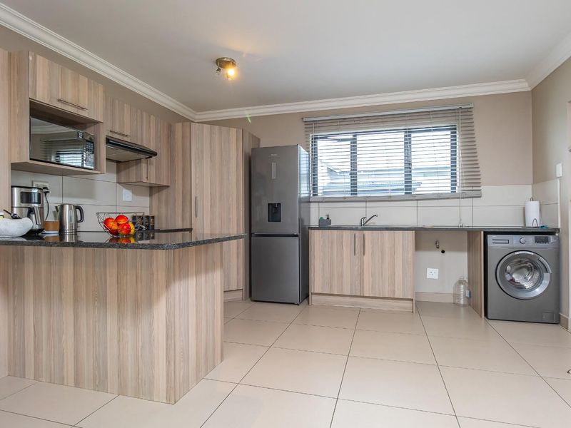 Modern kitchen featuring light wood-grain cabinetry, granite countertops, integrated microwave, extractor fan, and tiled flooring with space for laundry appliances.