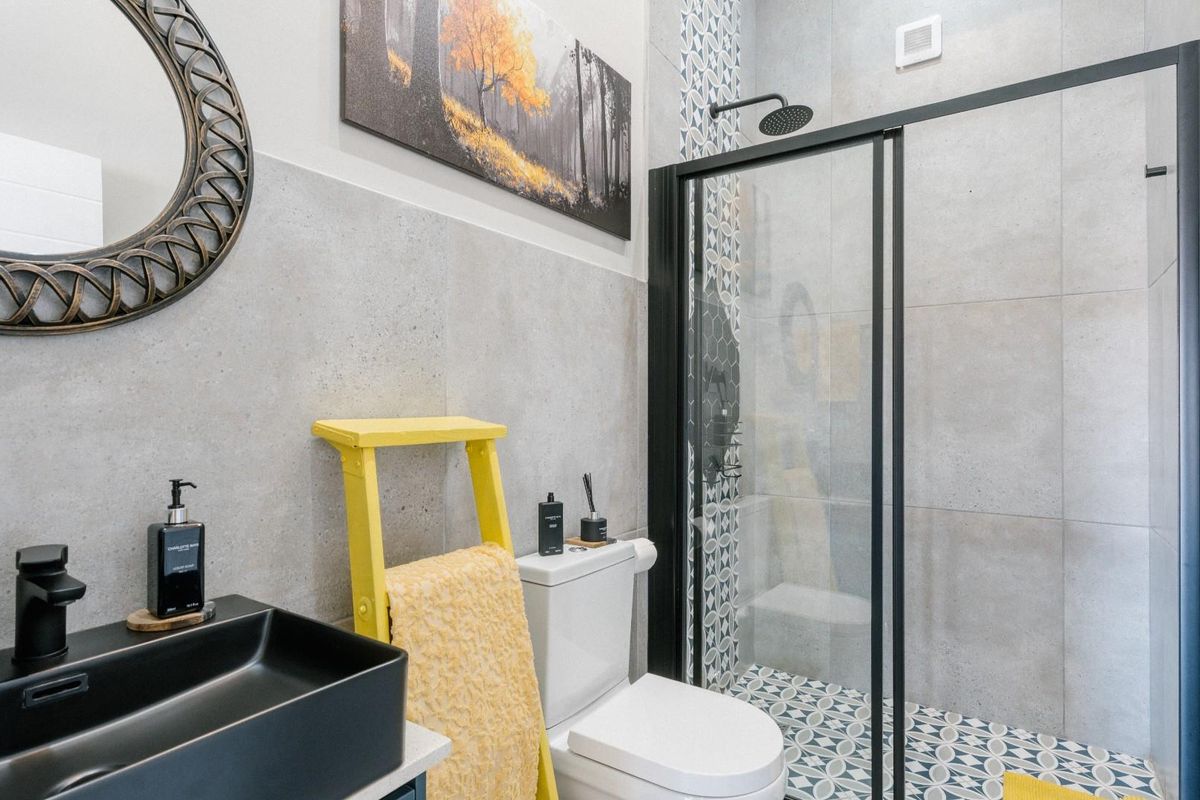 Modern bathroom featuring a walk-in shower with black frame, patterned floor tiles, wall-mounted basin, and contemporary grey wall tiling.