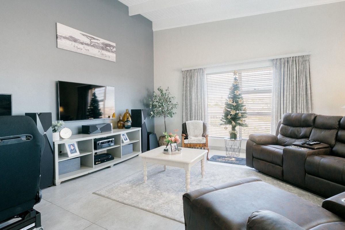 A spacious living room featuring high ceilings, large windows with blinds, and neutral tiled flooring, creating a bright and comfortable atmosphere.