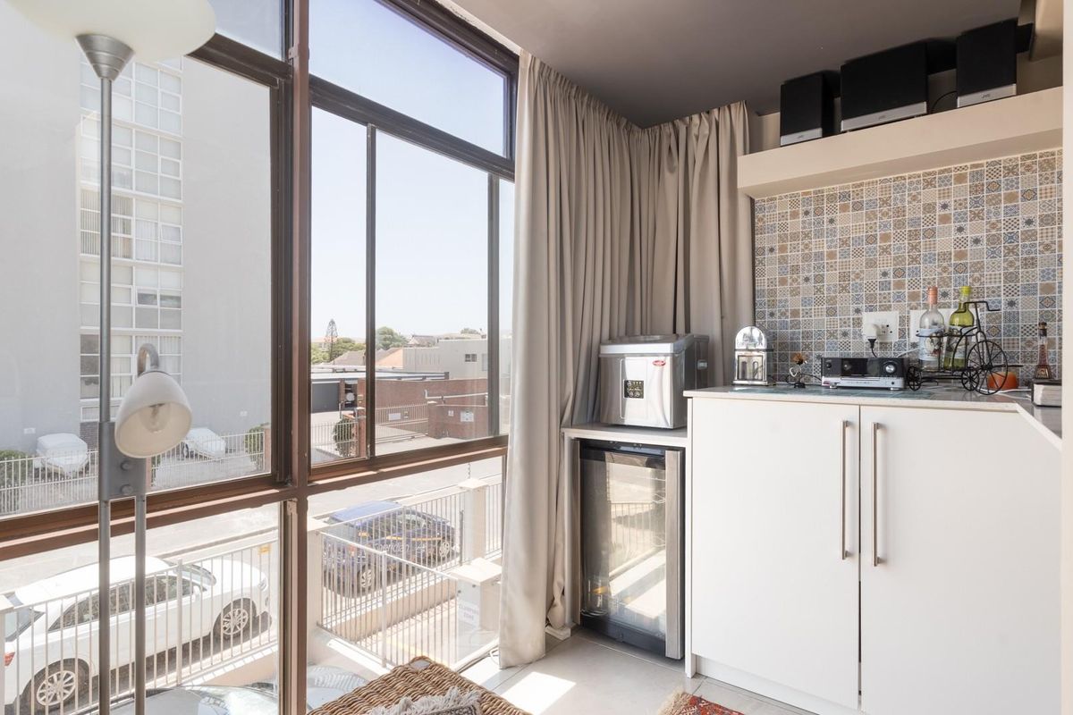 A compact kitchenette area featuring built-in cabinetry, decorative tiled backsplash, and large windows providing natural light and an urban street view.