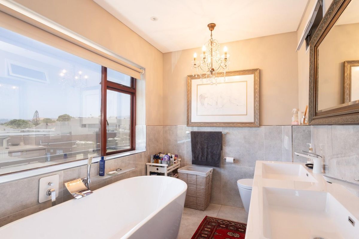 Modern bathroom featuring a freestanding bathtub, double vanity with integrated sinks, large window, and elegant chandelier lighting.