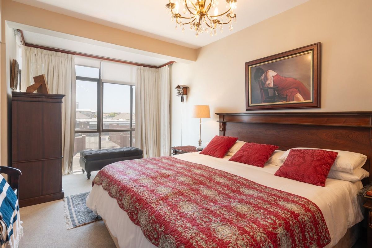 A well-maintained bedroom featuring large windows with natural light, neutral carpeting, and a classic chandelier fixture.