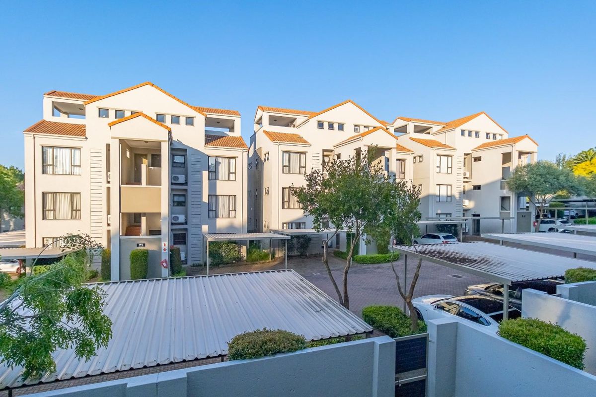 Exterior view of a multi-story apartment complex featuring tiled roofs, paved parking areas with carports, and landscaped grounds.