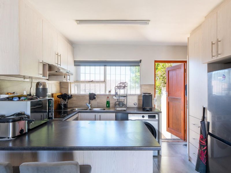 A functional kitchen featuring light wood-look cabinetry, dark countertops, integrated appliances, and direct access to an outdoor area.