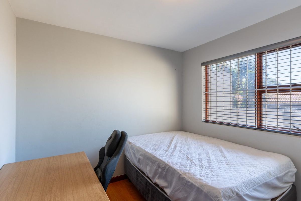 A functional bedroom featuring laminate flooring, neutral wall finishes, and a window fitted with timber-framed venetian blinds.