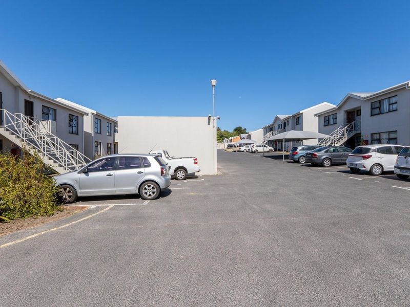 Exterior view of an apartment complex featuring paved parking areas, external staircases, and residential building facades under a clear sky.
