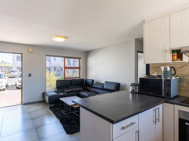 Open-plan living area featuring a modern kitchen with built-in cabinetry, oven, and hob, seamlessly flowing into a lounge space with direct exterior access.