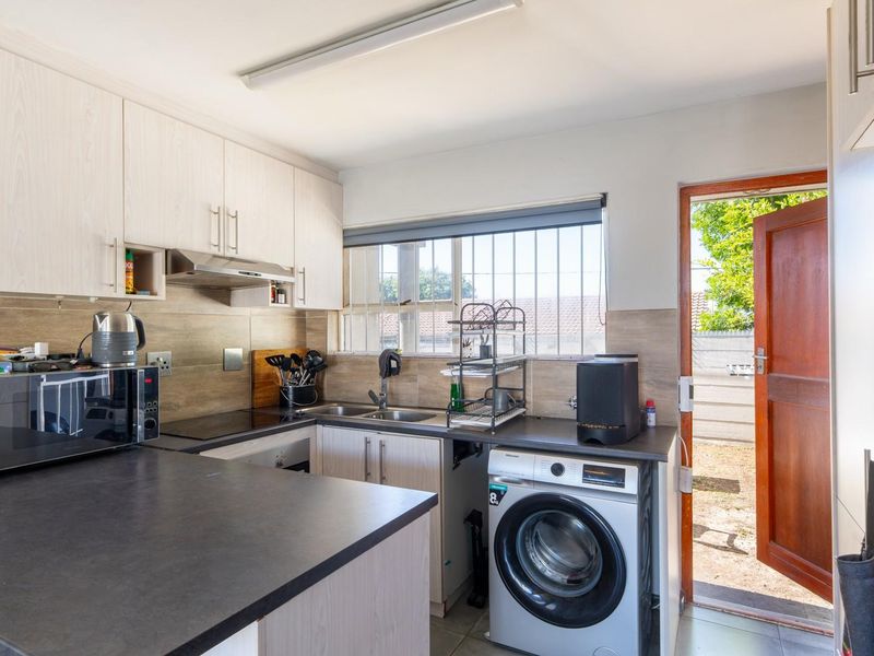 Functional kitchen featuring light wood-look cabinetry, dark countertops, integrated laundry plumbing, and direct access to the rear exterior area.
