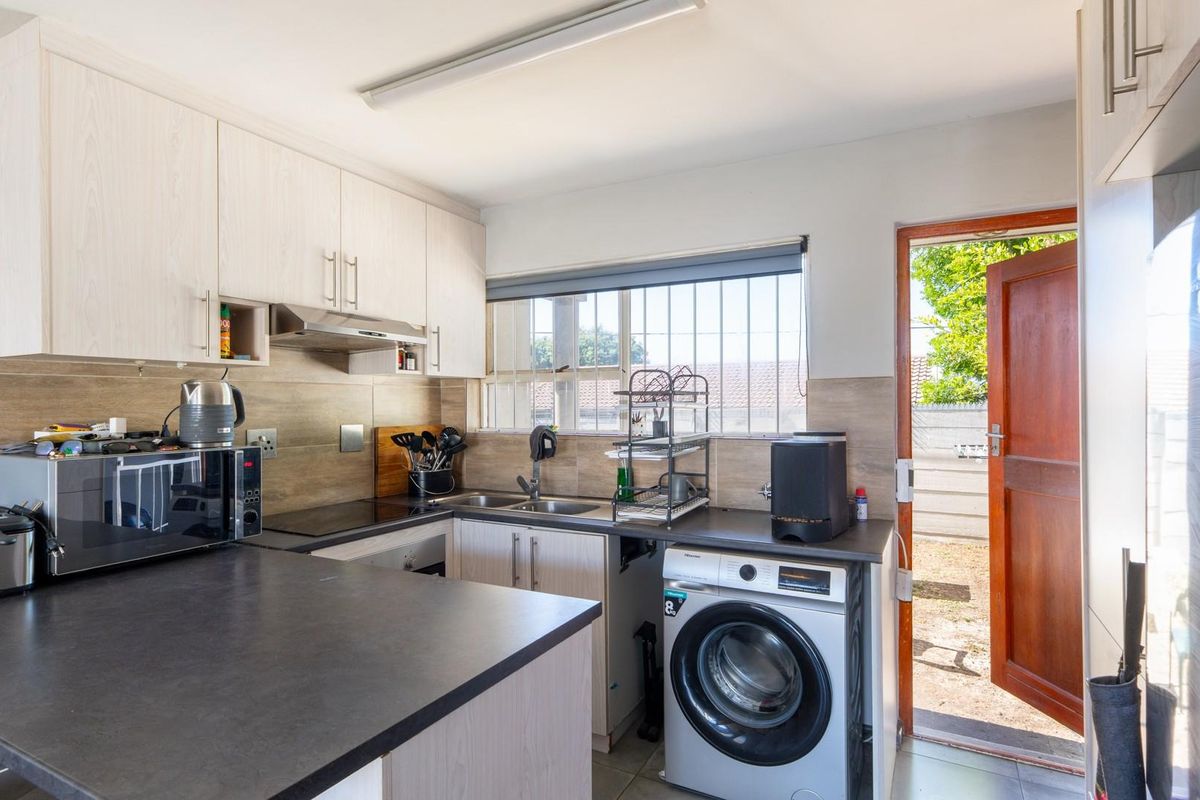 Functional kitchen featuring light wood-look cabinetry, dark countertops, integrated laundry plumbing, and direct access to the rear exterior area.