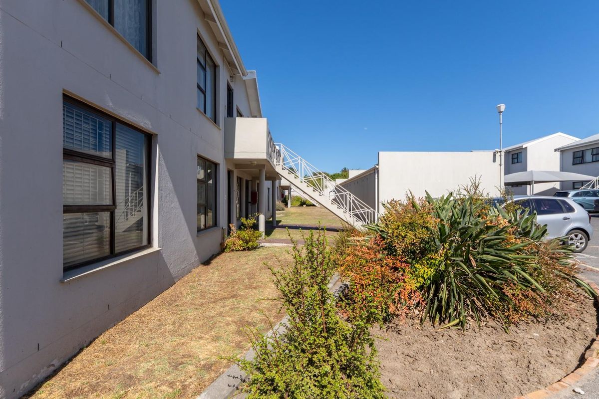 Exterior view of the apartment complex featuring a rear facade, external staircase, balcony, and adjacent paved parking area.