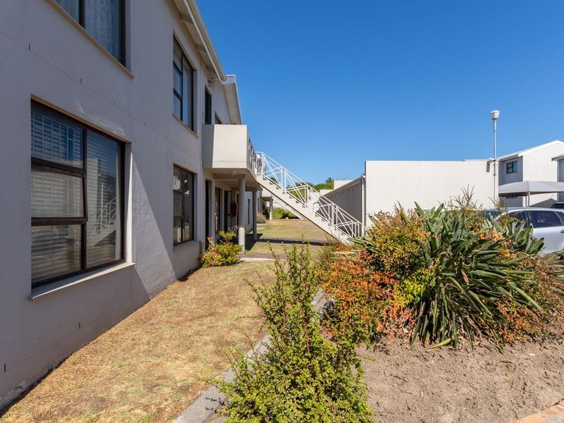 Exterior view of the apartment complex featuring a rear facade, external staircase, balcony, and adjacent paved parking area.
