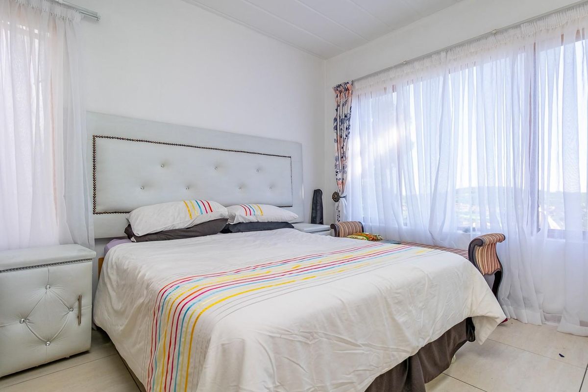 A bright bedroom featuring large windows with sheer curtains, tiled flooring, and a built-in headboard area.