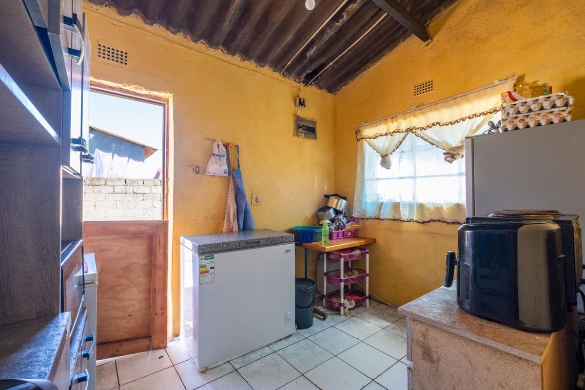 A functional kitchen or utility space featuring tiled flooring, exposed roof structure, and direct access to the exterior.