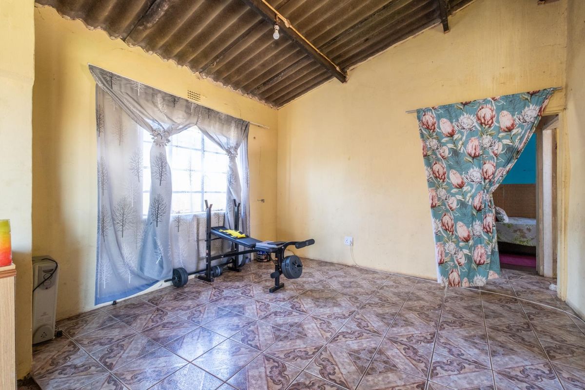 A basic bedroom featuring tiled flooring, exposed corrugated roof structure, and a window with natural light.