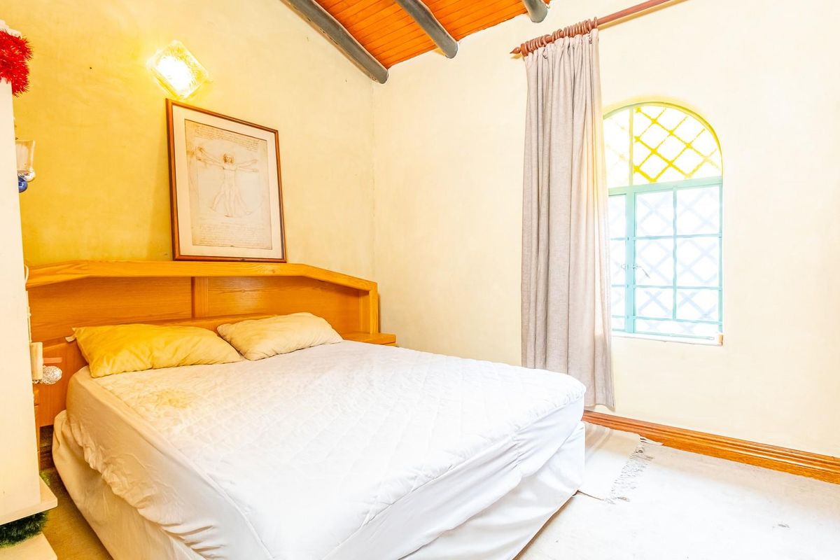 A bedroom featuring a vaulted timber ceiling, built-in wooden headboard, and an arched window with decorative metal security bars.