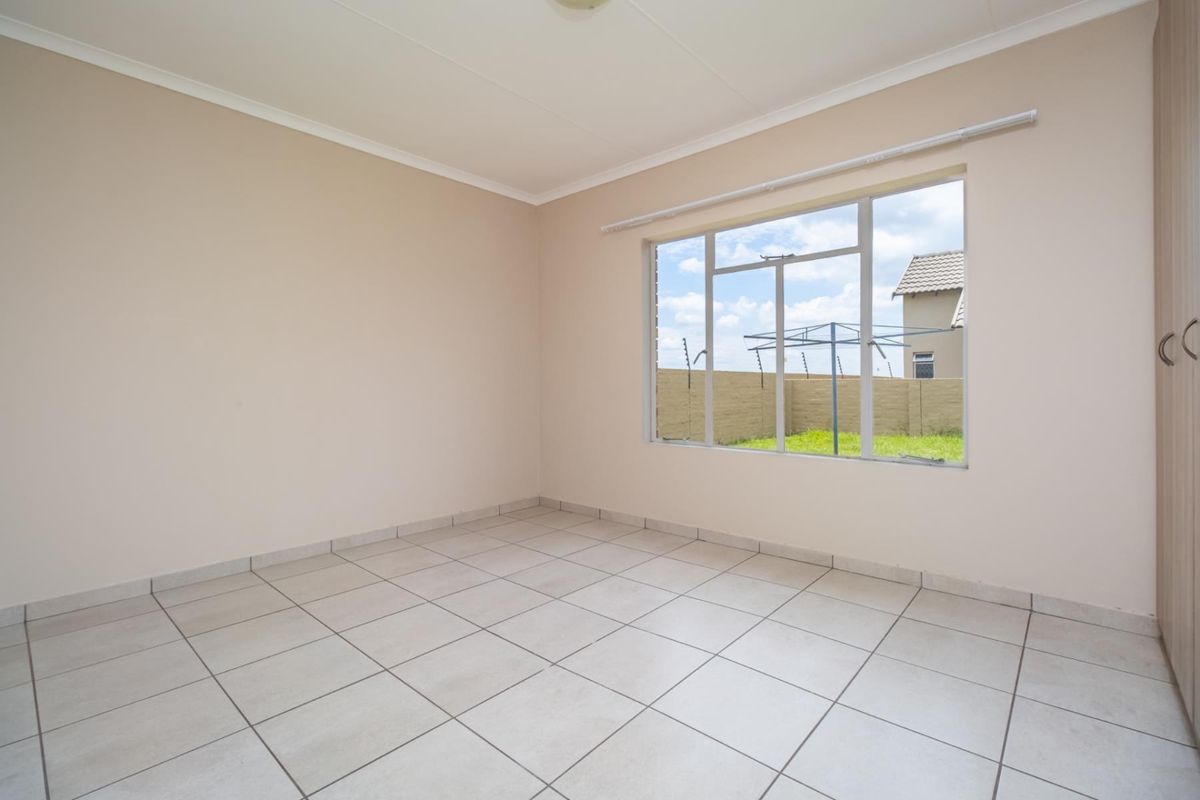 A bright, empty bedroom featuring neutral wall paint, tiled flooring, and a large window overlooking the rear garden area.