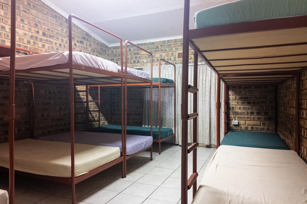 A dormitory-style bedroom featuring exposed brick walls, tiled flooring, and multiple metal bunk bed frames.