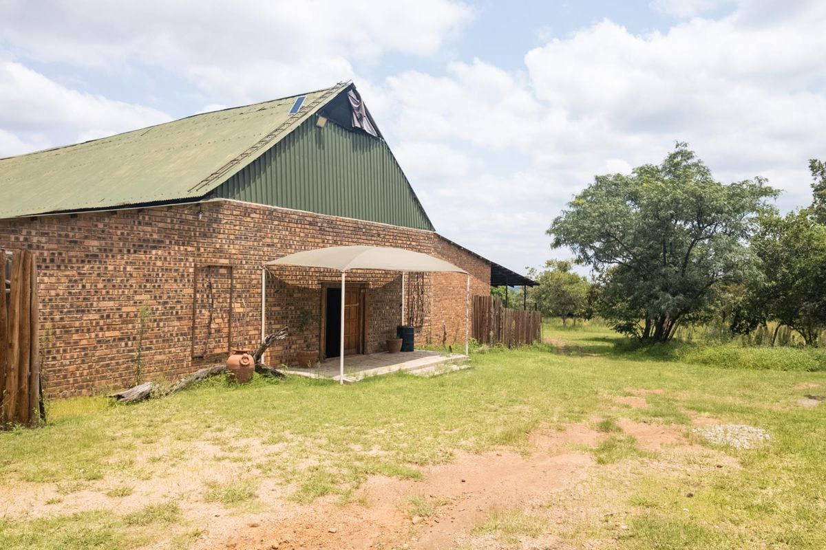 Exterior view of a rustic brick farm building featuring a green metal roof and a covered entrance patio area.