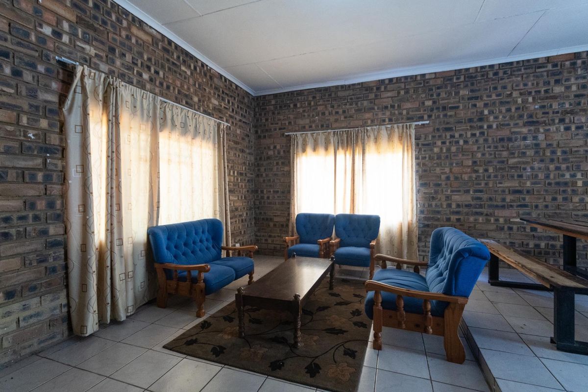A spacious living area featuring exposed face-brick walls, tiled flooring, and large windows allowing for natural light.