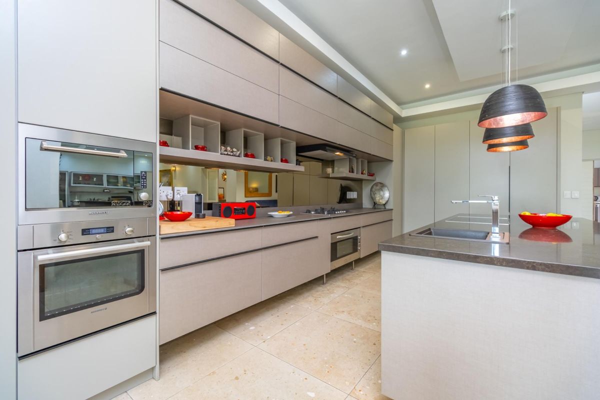 Modern kitchen featuring sleek cabinetry, integrated stainless steel appliances, a central island with a sink, and a mirrored backsplash.