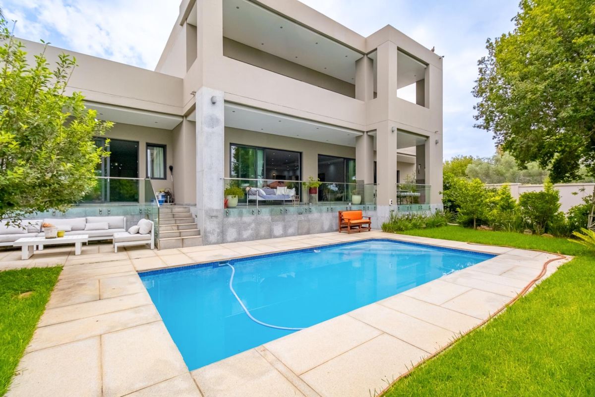 Modern double-story residence featuring a spacious covered patio, glass balustrades, and a well-maintained swimming pool set within a landscaped garden.