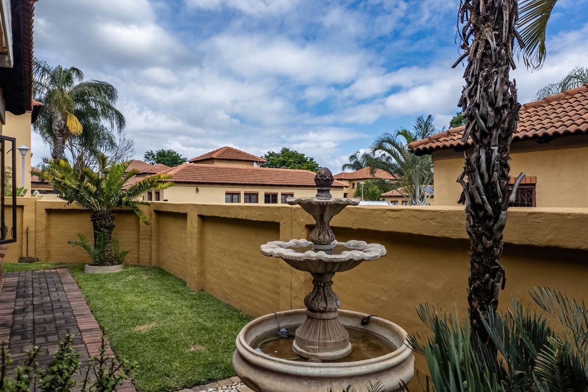 A private rear garden area featuring a stone water fountain, paved walkway, and perimeter walling within a residential estate setting.