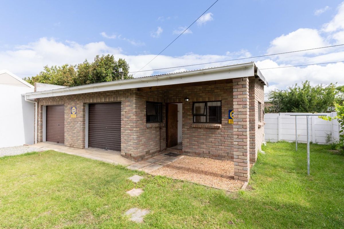 A detached brick-built structure featuring two roller garage doors and a side entrance, set within a private garden area.