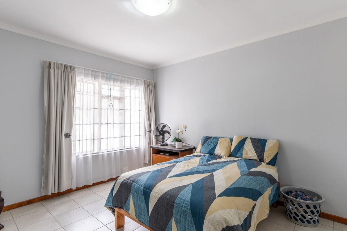 A well-lit bedroom featuring tiled flooring, neutral wall tones, and a large window with fitted curtain tracks.