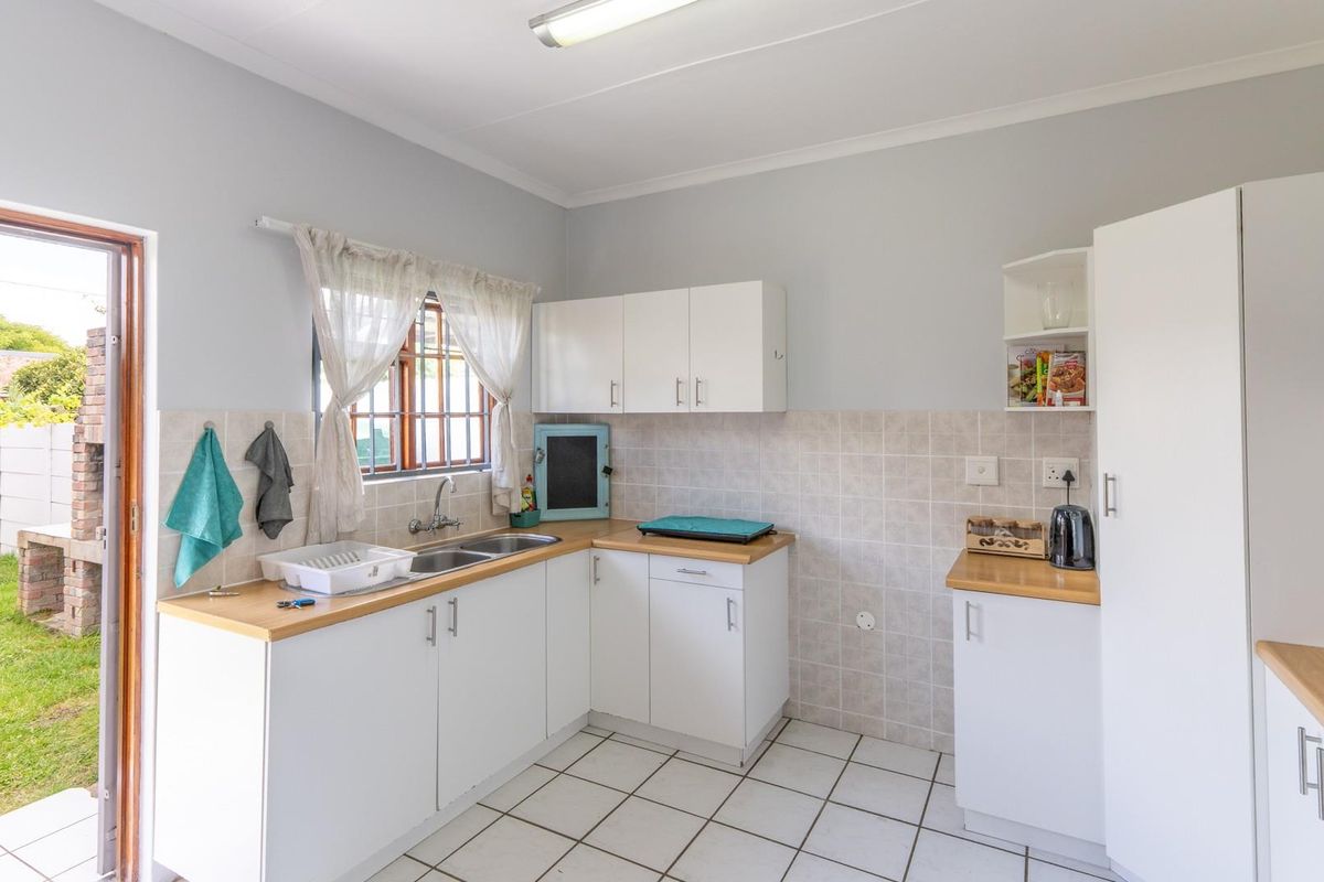 A functional kitchen featuring white cabinetry, light wood-look countertops, tiled splashbacks, and direct access to the rear garden.