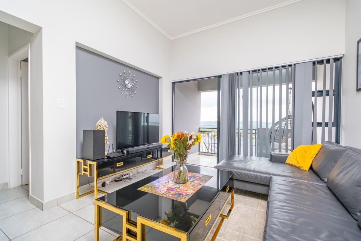 A bright living room featuring a recessed feature wall, tiled flooring, and large sliding glass doors providing access to a balcony.