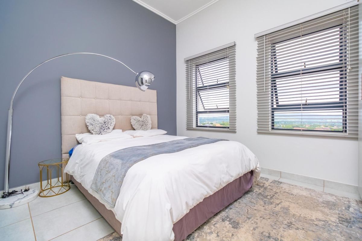 A well-maintained bedroom featuring an accent wall, tiled flooring, and dual windows fitted with venetian blinds.