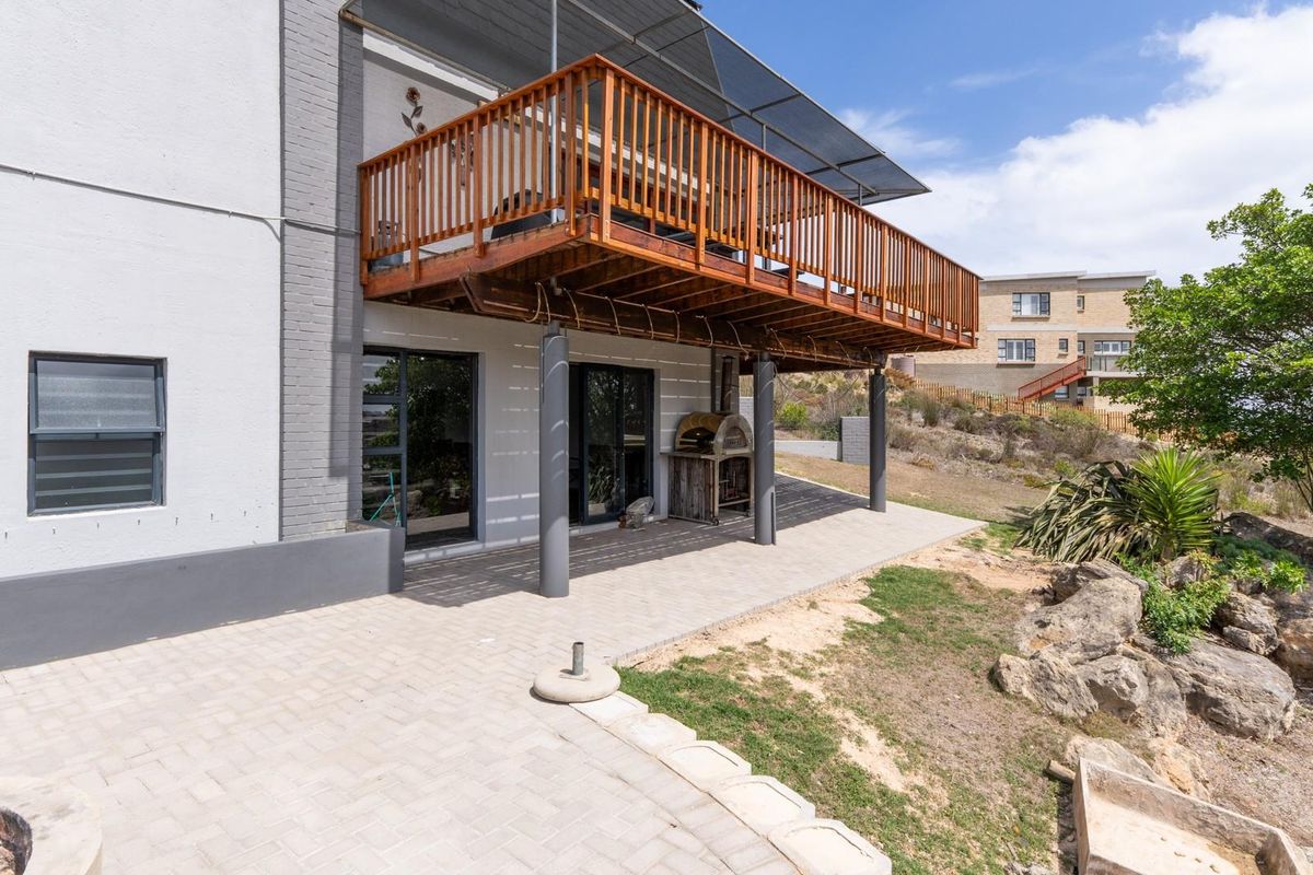 Rear exterior view featuring a paved patio area, a raised wooden balcony with railing, and a built-in outdoor pizza oven.