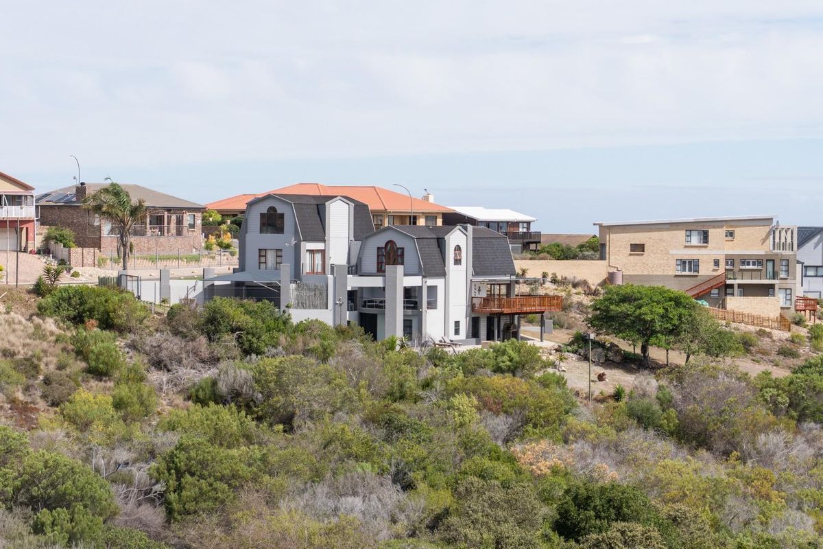 An elevated view of a multi-story residential property featuring a balcony and pitched roof, situated within a landscaped coastal or hillside neighborhood.