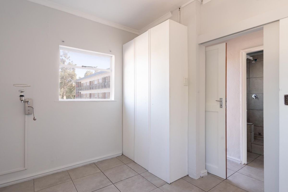 A bedroom featuring built-in cupboards, tiled flooring, and an en-suite bathroom access.