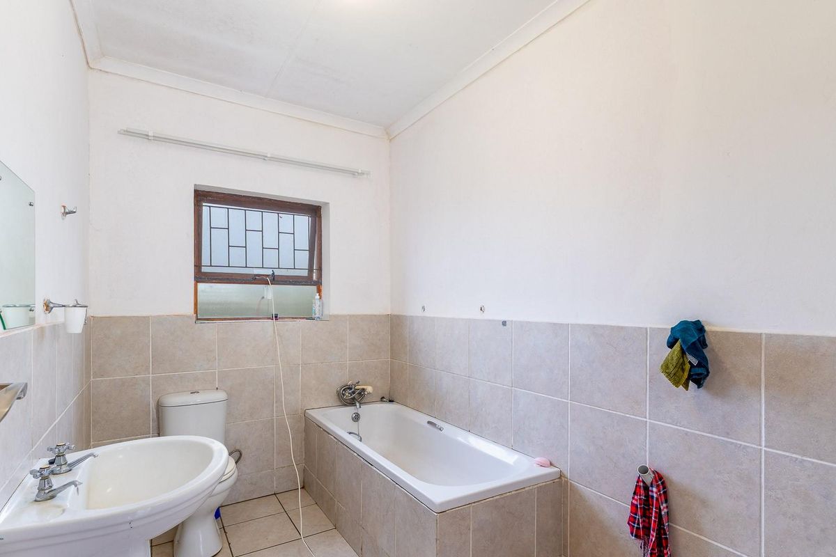 A functional bathroom featuring a standard bathtub, pedestal basin, and tiled walls with a security-barred window.