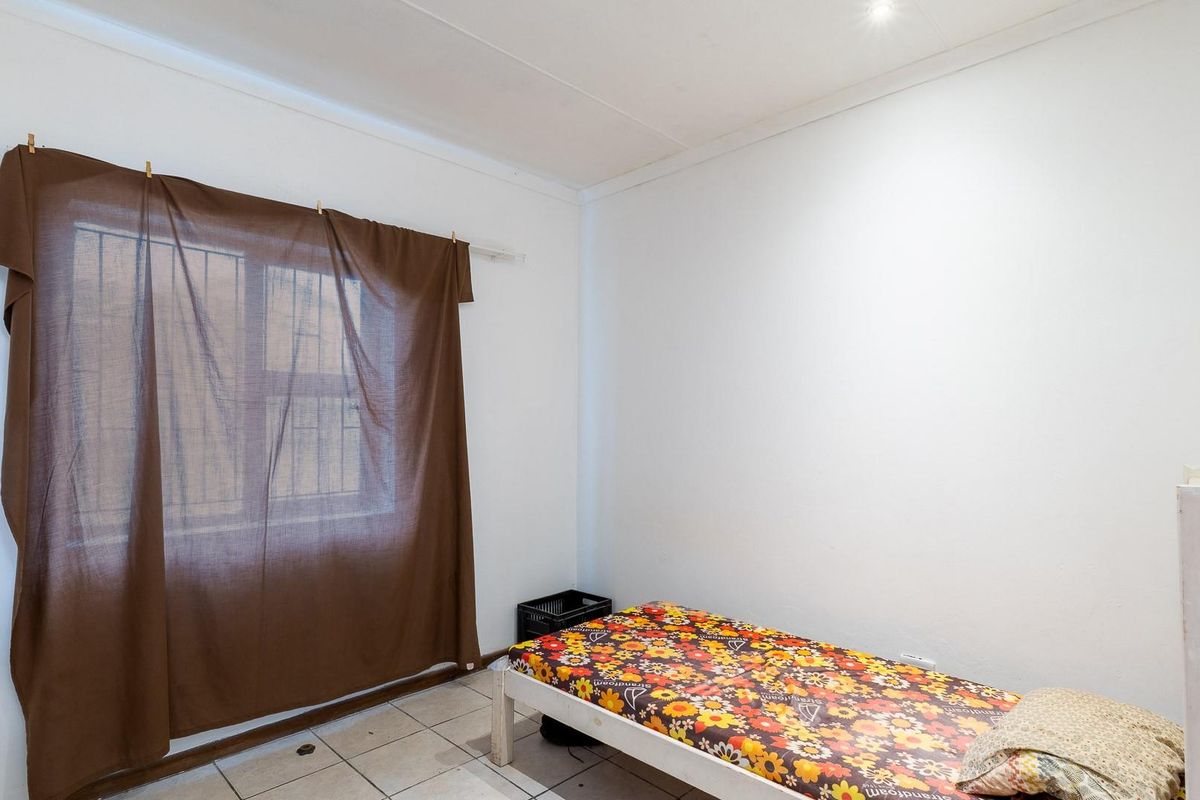 A simple bedroom featuring tiled flooring and a window with security bars, offering a functional space ready for updates.